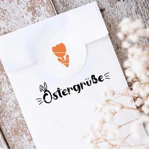 May include: White card with a black bunny and the text "Ostergr&uuml;&szlig;e" in black script. A small orange flower is in the upper left corner.