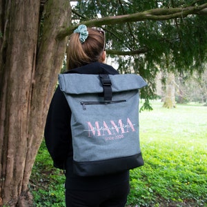 May include: A gray backpack with a black roll-top closure and a pink embroidered design that says "Mama since 2008".