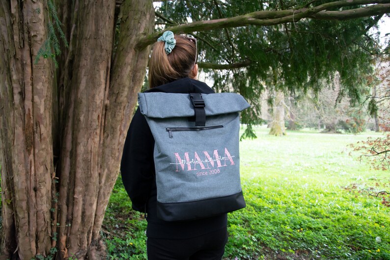 May include: A gray backpack with a black roll-top closure and a pink embroidered design that says "Mama since 2008".