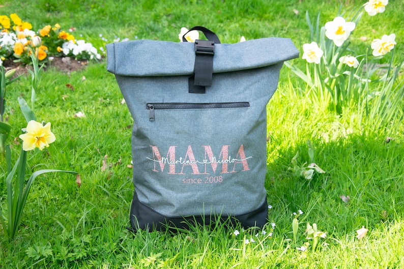 May include: Gray and black roll-top backpack with a zippered pocket and a pink glitter design that says "MAMA Martina & Nicola since 2008".