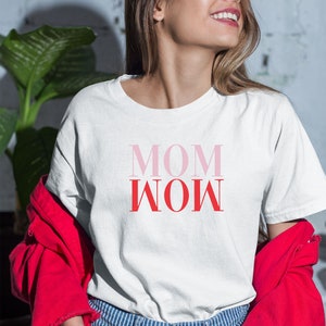 Può includere: Maglietta bianca con la scritta "MOM WOW" stampata in rosa e rosso.