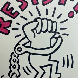 May include: Black and white illustration of a figure breaking free from shackles, with the word "RESIST" in pink above. The figure has a raised fist, radiating lines, and is in motion.