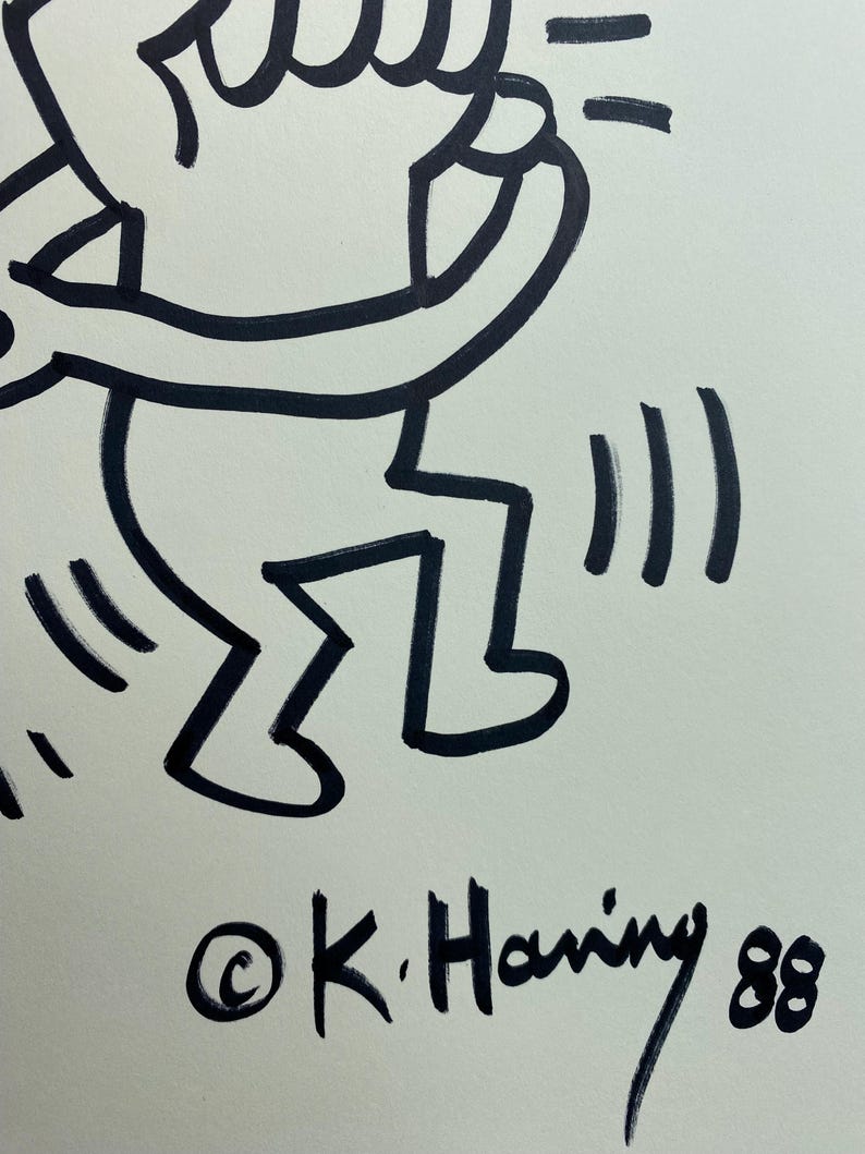 May include: Black and white line drawing of a dancing figure with raised arms. The artwork is signed "&copy;K. Haring 88" in black ink. The figure has a simple, bold outline, and the style is reminiscent of street art.
