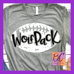 Pode incluir: Camiseta cinza com um design de bola de futebol branco e o texto "Wolf Pack" em preto. O design tem um visual envelhecido.