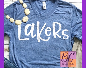May include: A blue t-shirt with the word "Lakers" written in white cursive lettering. The shirt is made of a soft, comfortable material and is perfect for showing your team spirit.