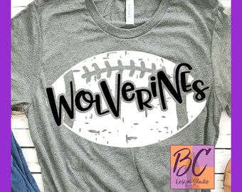 May include: Gray t-shirt with a white football graphic and the text "WOLVERINES" in black. The shirt is on a white wooden surface.