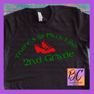 May include: Black t-shirt with green text that reads "There's No Place Like 2nd Grade" and a pair of red glitter shoes.