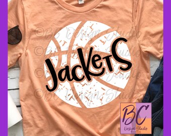 Op de afbeelding: Een perzikkleurig T-shirt met een witte basketbal afbeelding en de tekst "Jackets" in zwart. De basketbal heeft een verweerde look en de tekst is in handschrift.