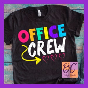 May include: Black t-shirt with the text "Office Crew" in rainbow colors with a yellow arrow pointing to the right and three pink hearts. The text "BC Design Studio" is in the bottom right corner.