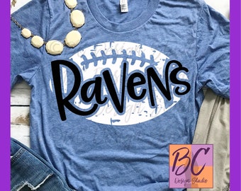 May include: A blue t-shirt with a white football design and the word "Ravens" in black lettering.