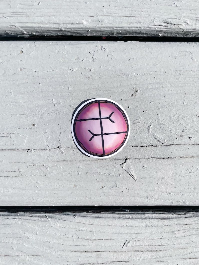 Puede incluir: Una pegatina redonda con borde blanco. Presenta un fondo degradado rosa y morado con un dise&ntilde;o geom&eacute;trico negro. La pegatina est&aacute; colocada sobre una superficie de madera gris y desgastada.
