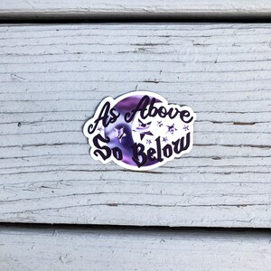 May include: A sticker with a purple and white moon and stars with the text "As Above So Below" in black.
