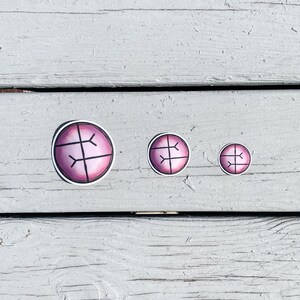 Puede incluir: Tres pegatinas con un dise&ntilde;o rosa y negro. Las pegatinas son circulares con un contorno negro y un centro rosa. Un gr&aacute;fico negro que se asemeja a una ret&iacute;cula est&aacute; en el centro de cada pegatina. Las pegatinas son de diferentes tama&ntilde;os.