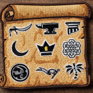 Op de afbeelding: Geborduurde patch in de vorm van een rol met diverse zwart-witte symbolen. Bevat een maan, een kroon en een palmboom. De patch heeft een beige achtergrond met een bruine rand.