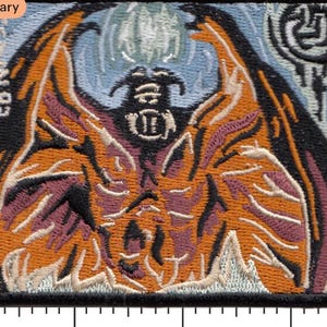 Puede incluir: Parche bordado con un diseño de criatura estilizada en naranja, morado y negro. El diseño incluye una figura alada con un rostro detallado y el texto "EDVIN 92". El fondo es azul claro y el borde es negro.