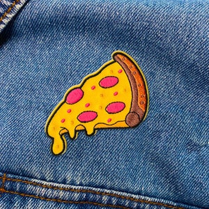 May include: An embroidered patch shaped like a slice of pizza with yellow melted cheese, pink pepperoni circles, and a brown crust edge. The patch is attached to a blue denim fabric surface with visible orange stitching along the bottom seam.