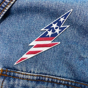 May include: A white lightning bolt patch with red and white stripes, resembling the American flag, sewn onto a blue denim jacket.
