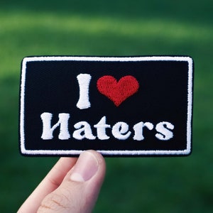 Könnte beinhalten: Schwarzer Patch mit weißen Nähten und dem Text "I love haters" in Weiß mit einem roten Herzen in der Mitte.