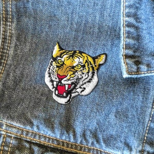 May include: A yellow, black, and white embroidered tiger head patch. The tiger has a fierce expression with its mouth open and teeth showing.
