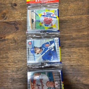 Puede incluir: Tres paquetes sin abrir de cromos de béisbol Fleer de 1989. Cada paquete contiene 42 cromos y 3 pegatinas con el logotipo. El paquete superior tiene un encabezado amarillo y rojo con el año y el nombre de la marca. El paquete del medio presenta a Ryne Sandberg.
