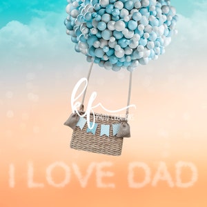 May include: A blue and silver balloon hot air balloon with a wicker basket and hessian sacks hanging from it. The balloon is floating in a blue and orange sky with white clouds. The words "I LOVE DAD" are written in white clouds below the balloon.