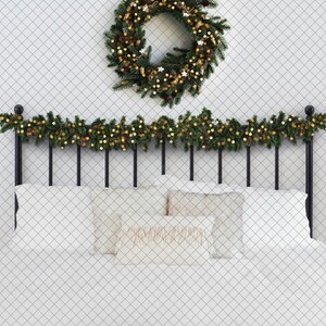 May include: A black metal bed frame with a white headboard and white bedding. A green garland with gold lights is draped across the headboard. A green wreath with gold lights and ornaments is hanging on the wall above the bed.