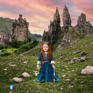以下が含まれることがあります： 青と金のドレスを着て、赤い髪と王冠をつけた少女が草地の中に立っています。中世のお城と岩山が夕焼け空の下に背景としてあります。画像には「KF PHOTO CREATIONS」というテキストが入っています。