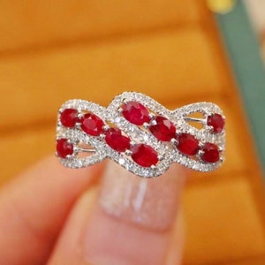May include: A silver ring with a wavy design set with oval-shaped red rubies and small white diamonds.