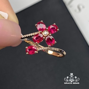 Puede incluir: Un anillo de oro con un diseño de flor de rubí. La flor tiene cinco pétalos, cada uno engastado con una piedra de rubí. El anillo tiene una banda delicada con pequeños diamantes.