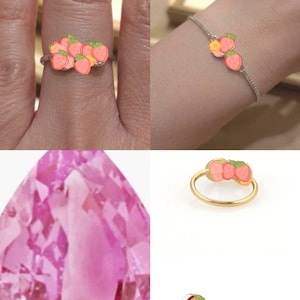 May include: A silver ring and a matching silver chain bracelet, both featuring a cluster of small, pink, strawberry-shaped charms with green leaves. Also includes a gold-toned ring with the same strawberry charm design and a large, faceted pink gemstone.