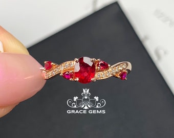 Op de afbeelding: Een ring van roségoud met een grote ovale robijn, omringd door kleinere robijnen en diamanten. De ring heeft een gedraaid bandontwerp.