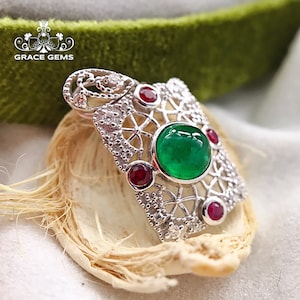 May include: A silver pendant with a large green emerald gemstone surrounded by smaller red rubies and white diamonds. The pendant is in a delicate filigree design.