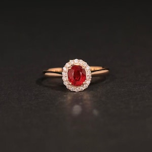 Può includere: Un anello in oro rosa con una pietra ovale rossa circondata da un'aureola di diamanti più piccoli.