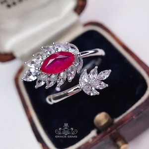 May include: A silver ring with a large, red marquise-shaped ruby surrounded by smaller, clear diamonds. The ring is set in a leaf-like design.