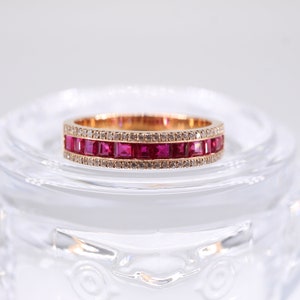 May include: A gold band ring with a double row of square-shaped ruby stones and a row of smaller diamonds.