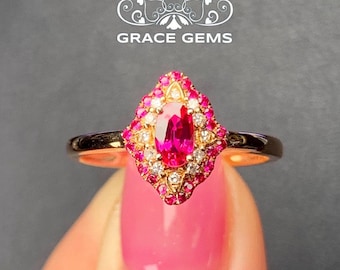 Op de afbeelding: Een gouden ring met een grote ovale robijn, omringd door kleinere diamanten en roze saffieren. De ring is gezet in een delicaat, versierd ontwerp.