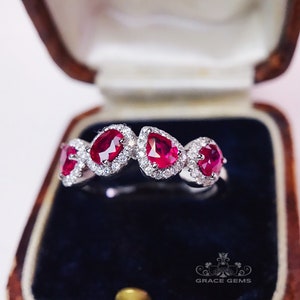 May include: A silver ring featuring five pear-shaped red rubies set in a halo of white diamonds.