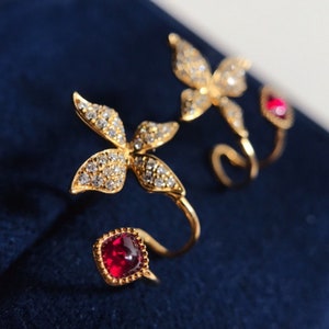 May include: A pair of gold-tone earrings featuring a butterfly design with clear rhinestones and a red gemstone accent.