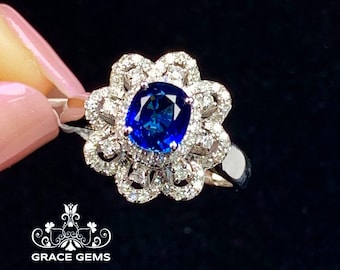 May include: A silver ring with a large blue sapphire surrounded by a halo of smaller diamonds. The ring has a floral design with intricate details.