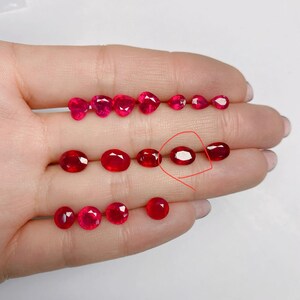 May include: A collection of vibrant red gemstones in various shapes, including oval, heart, and round cuts. The gemstones are displayed on a light background, showcasing their rich color and clarity. The arrangement highlights the different sizes and styles of the gemstones.