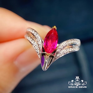 May include: A marquise-shaped ruby ring set in a white gold band with a V-shaped design. The ring is accented with small diamonds on the band.