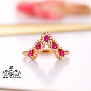 May include: A gold ring with a V-shaped design set with five pear-shaped ruby gemstones and smaller round diamonds.