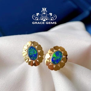 May include: A pair of gold earrings with a blue and green opal gemstone set in a floral design. The earrings are on a white fabric background.