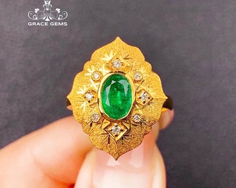 May include: A gold ring featuring a large green emerald gemstone surrounded by smaller diamonds. The ring has a detailed, ornate design.