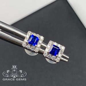 May include: A pair of square-shaped earrings with a blue sapphire center stone surrounded by a halo of smaller diamonds.