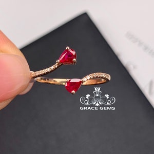 May include: A delicate gold ring with two pear-shaped ruby gemstones and a row of small diamonds. The ring is designed to wrap around the finger.