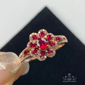 May include: A rose gold ring with a large oval ruby surrounded by smaller rubies and diamonds. The ring has a floral design.