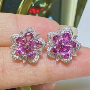 Pu&ograve; includere: Un paio di orecchini d'argento a forma di fiore con pietre preziose rosa e pietre preziose trasparenti pi&ugrave; piccole.
