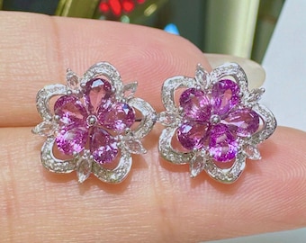 May include: A pair of silver flower-shaped earrings with pink gemstones and smaller clear gemstones.