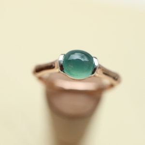 May include: A green gemstone ring with a silver setting and a rose gold band.